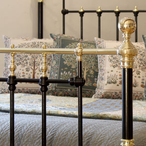 Close-up of a bed with black metal frame and gold accents, featuring floral-patterned pillows.