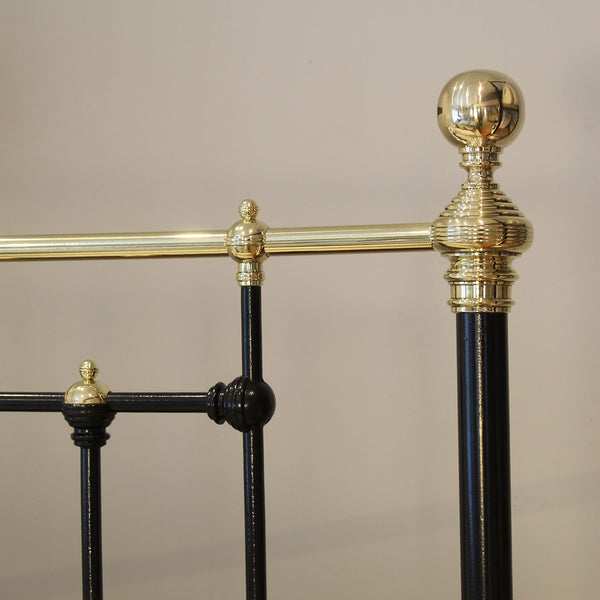 Close-up of a black metal bed frame with gold accents against a beige background