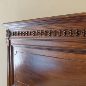 Close-up of a wooden headboard with intricate carvings against a beige wall.