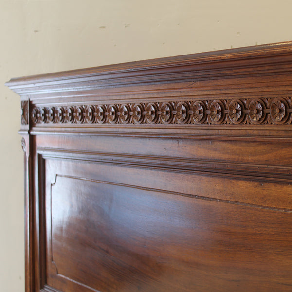 Close-up of a wooden headboard with intricate carvings against a beige wall.