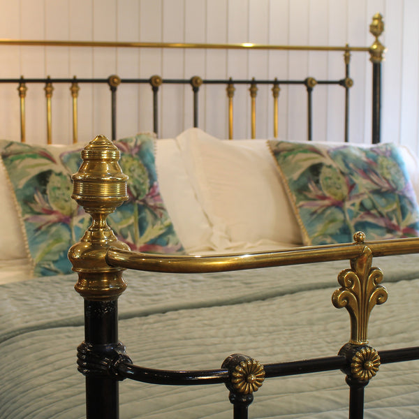 Close-up of an ornate bed frame with polished brass and black metal details, styled with patterned green and white pillows and a light green quilted bedspread in a bedroom setting.