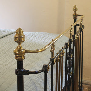 An ornate vintage-style metal bed frame with polished brass rails and finials, paired with black iron side rails, shown with a light-colored quilted bedspread.