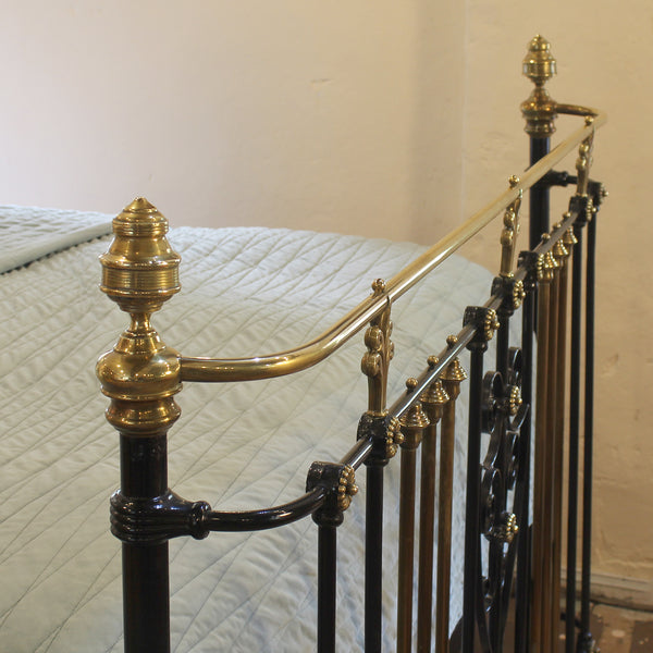 An ornate vintage-style metal bed frame with polished brass rails and finials, paired with black iron side rails, shown with a light-colored quilted bedspread.