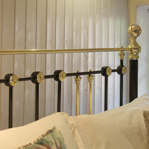 Close-up of a bed frame with black and gold metal bars, pillows, and a light wood-paneled wall in the background.