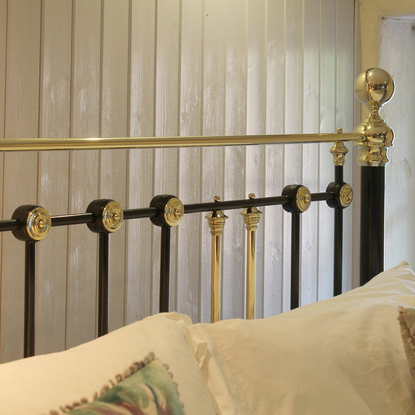 Close-up of a bed frame with black and gold metal bars, pillows, and a light wood-paneled wall in the background.