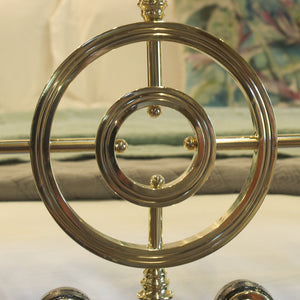 A close-up of a polished brass decorative nautical wheel or ship's wheel ornament with concentric rings and small brass finials, set against a softly blurred indoor background.