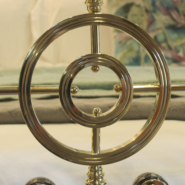 A close-up of a polished brass decorative nautical wheel or ship's wheel ornament with concentric rings and small brass finials, set against a softly blurred indoor background.