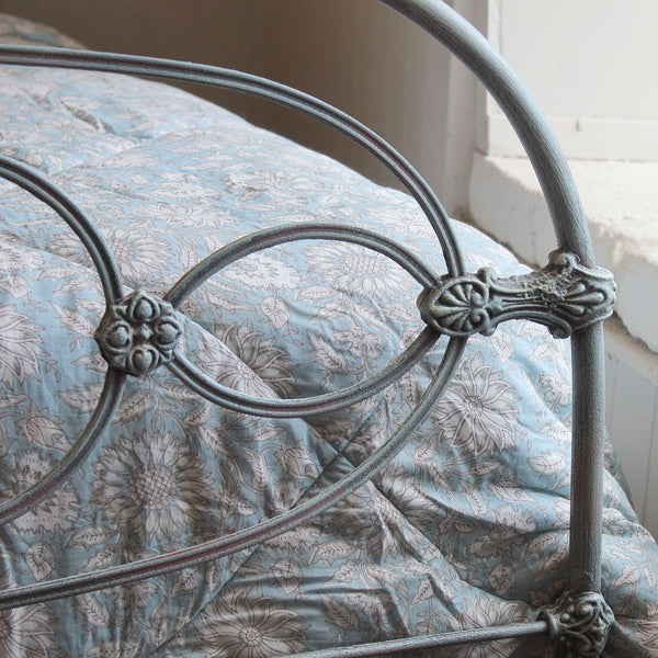 Close-up of a metal bed frame with decorative scrollwork and a blue floral-patterned bedding set beside it.