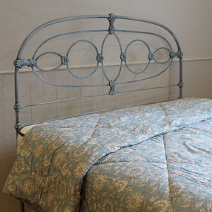 A light blue metal bed frame with an ornate scrollwork headboard, shown with a matching light blue and beige floral-patterned comforter.