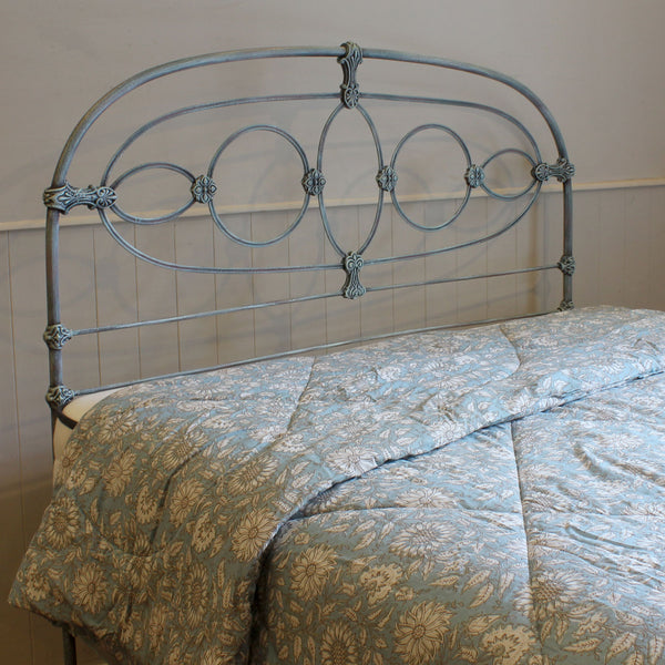 A light blue metal bed frame with an ornate scrollwork headboard, shown with a matching light blue and beige floral-patterned comforter.