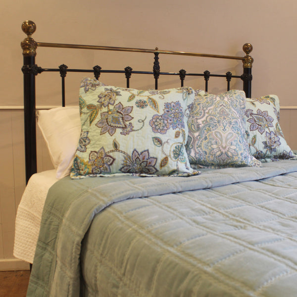 Bed with floral pillows and a green blanket against a beige wall.
