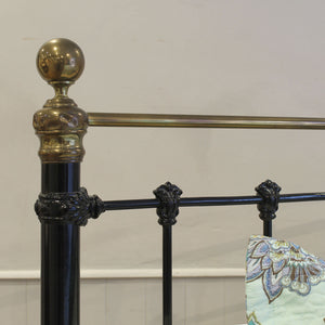 Close-up of a decorative metal bed frame with brass accents on a white background.