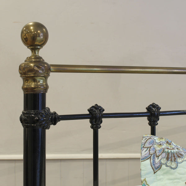 Close-up of a decorative metal bed frame with brass accents on a white background.