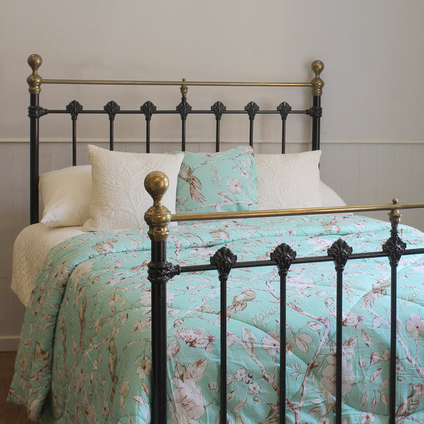 A bed dressed in a mint green floral quilt and matching pillow shams, styled with white pillows, set against a black metal bed frame with gold-toned accents in a bedroom setting.