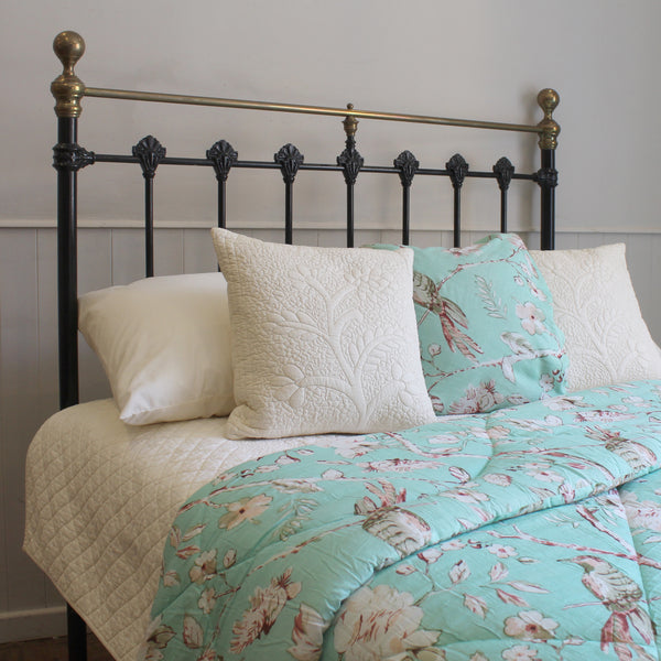 A bed dressed in a floral comforter and matching pillows, styled with cream quilts and pillows, set against a black metal headboard with brass accents.