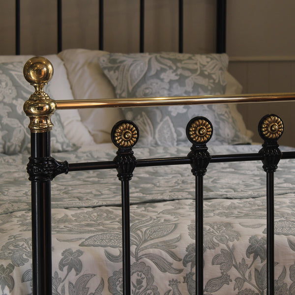 Close-up of a classic black metal bed frame with ornate gold-toned accents, shown with patterned bedding and pillows in a bedroom setting.