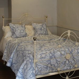 An antique bed dressed in a light blue and white floral toile patterned comforter and matching pillows, set against a neutral wall background.