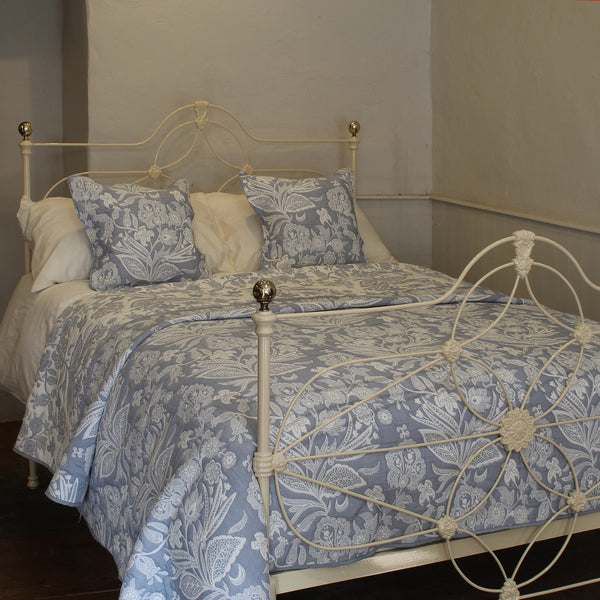An antique bed dressed in a light blue and white floral toile patterned comforter and matching pillows, set against a neutral wall background.