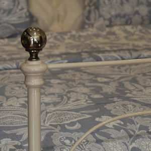 Close-up of a white metal antique bed frame post with a polished silver ball finial, set against a blue and white floral patterned bedding.