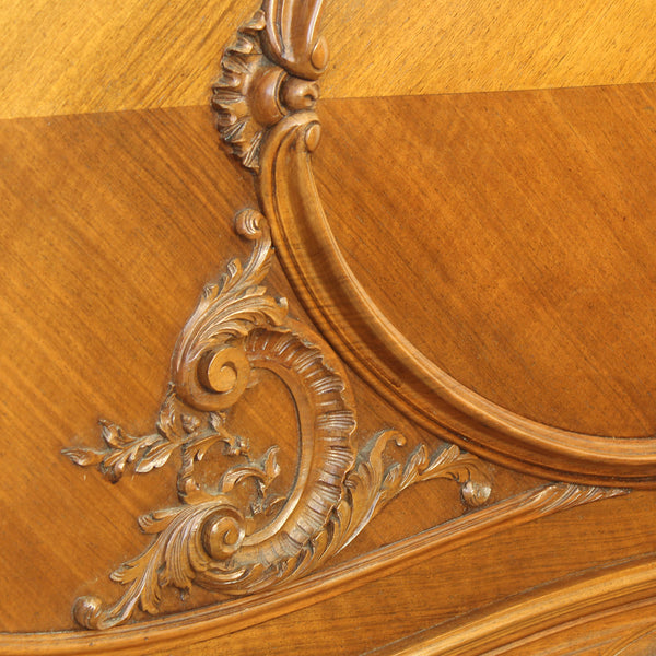 Close-up of an ornate carved wooden panel with a warm honey-toned wood grain and decorative scrollwork.