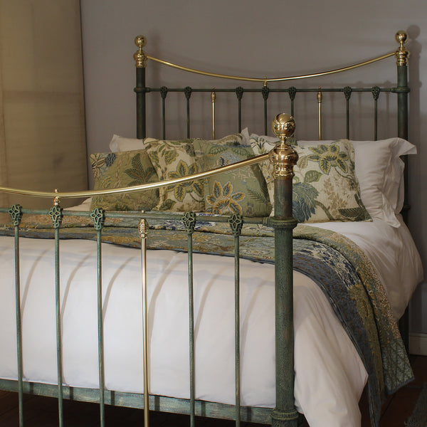 An ornate metal bed frame with a dark green painted finish and gold-toned accents, styled with white bedding and decorative floral pillows in a bedroom setting.