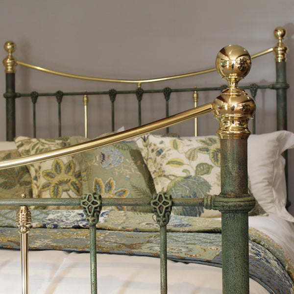 An ornate metal bed frame with a distressed green finish and polished gold accents, styled with patterned pillows and bedding in a bedroom setting.