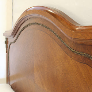 Close-up of a polished medium-brown wooden headboard with a curved top and decorative inlay, shown against a light wall.
