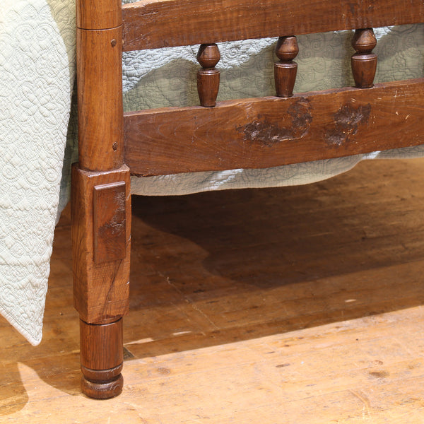 Close-up of a wooden bed frame with turned posts on a wooden floor.