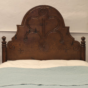 Wooden headboard with intricate carvings on a bed with a light blue and beige comforter.