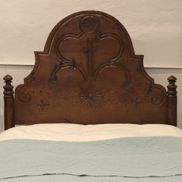 Wooden headboard with intricate carvings on a bed with a light blue and beige comforter.
