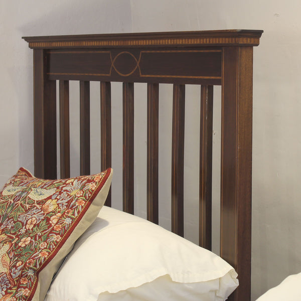 A dark brown wooden bed headboard with vertical slats and a decorative geometric inlay, shown with white pillows and a patterned accent pillow against a plain light gray wall.