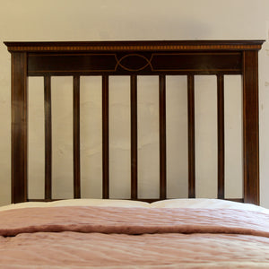 A dark brown wooden bed headboard with vertical slats and a decorative geometric inlay near the top, shown above a bed with a pink quilted comforter.