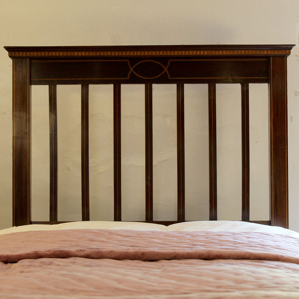 A dark brown wooden bed headboard with vertical slats and a decorative geometric inlay near the top, shown above a bed with a pink quilted comforter.