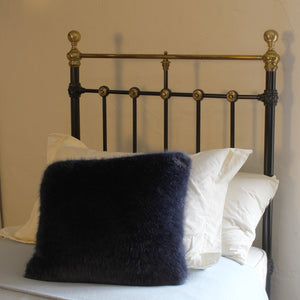 A dark navy blue faux fur throw pillow resting on a bed with white pillows and a black metal headboard with gold accents.